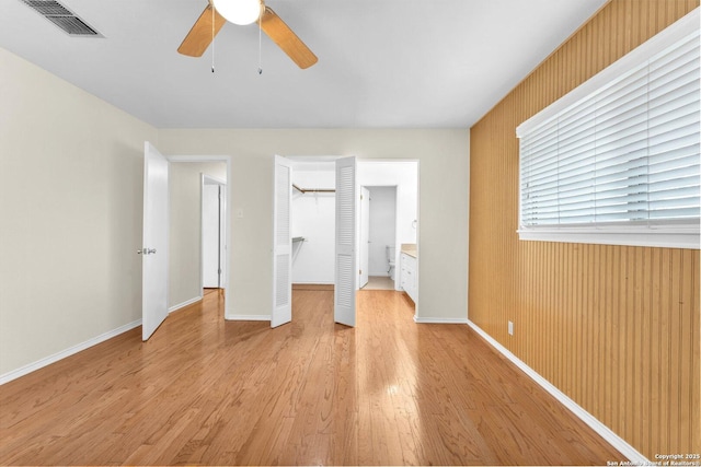 unfurnished bedroom featuring ceiling fan, a walk in closet, a closet, and light wood-type flooring