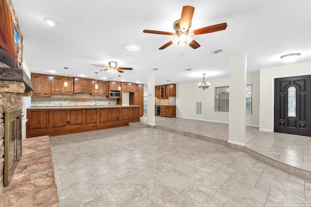 kitchen featuring built in microwave, a stone fireplace, decorative light fixtures, ceiling fan with notable chandelier, and backsplash