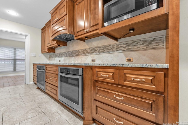 kitchen with tasteful backsplash, appliances with stainless steel finishes, light stone countertops, and light tile patterned flooring