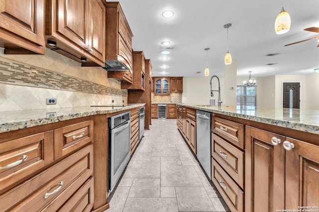 kitchen with pendant lighting, sink, appliances with stainless steel finishes, light stone countertops, and decorative backsplash