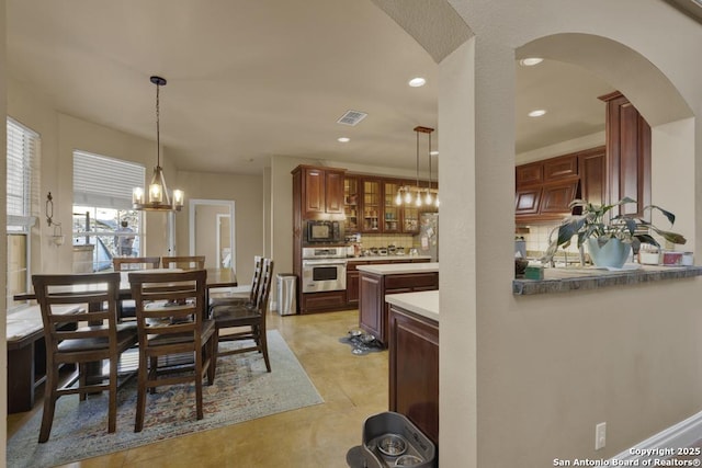 kitchen with appliances with stainless steel finishes, kitchen peninsula, a notable chandelier, pendant lighting, and backsplash