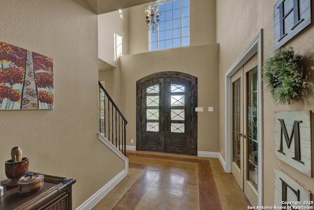 foyer featuring a towering ceiling, a wealth of natural light, a chandelier, and french doors