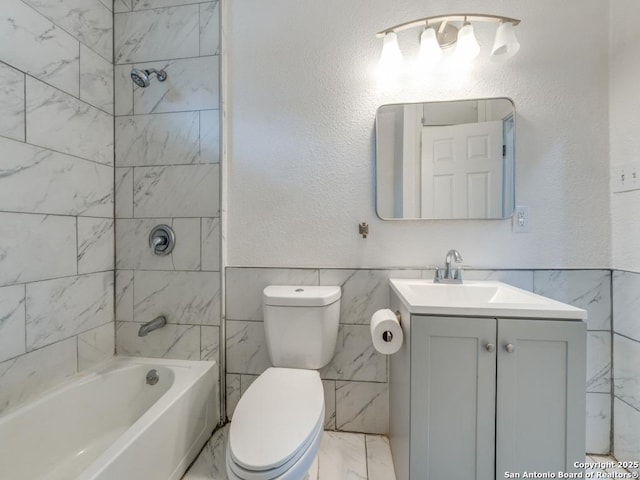 full bathroom featuring vanity, tiled shower / bath, tile walls, and toilet