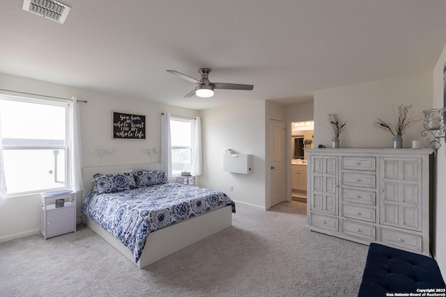 bedroom featuring light colored carpet, ceiling fan, and ensuite bath