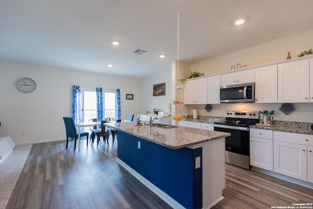 kitchen with stainless steel appliances, light stone countertops, a center island with sink, and white cabinets