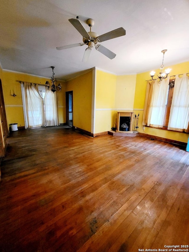 unfurnished living room featuring wood-type flooring, plenty of natural light, ornamental molding, and ceiling fan with notable chandelier