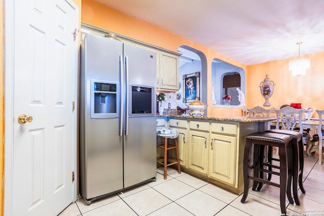 kitchen featuring a breakfast bar area, stainless steel fridge with ice dispenser, pendant lighting, dark stone counters, and cream cabinetry