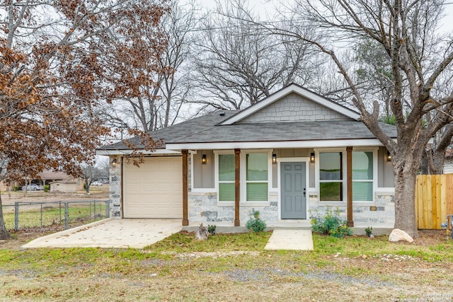 view of front facade with driveway, stone siding, fence, and roof with shingles