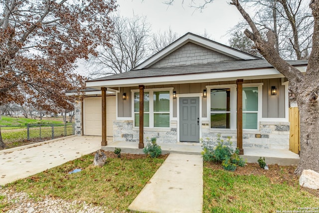 bungalow with covered porch, stone siding, board and batten siding, and driveway