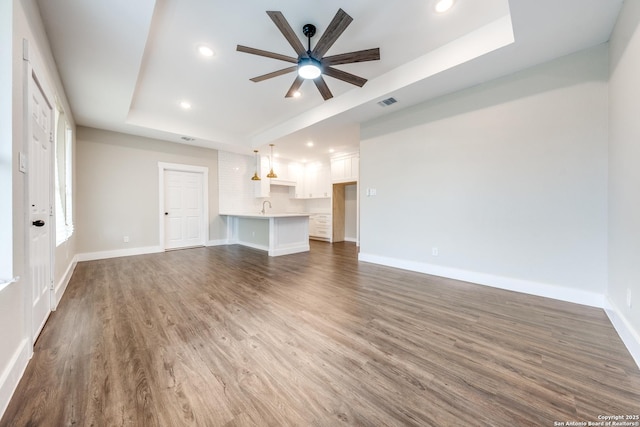 unfurnished living room with ceiling fan, sink, dark hardwood / wood-style flooring, and a tray ceiling