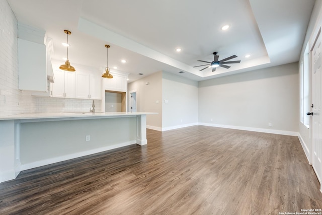 unfurnished living room with ceiling fan, a tray ceiling, and dark hardwood / wood-style flooring