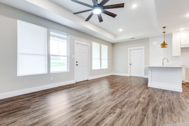 unfurnished living room featuring dark hardwood / wood-style flooring, sink, a raised ceiling, and ceiling fan