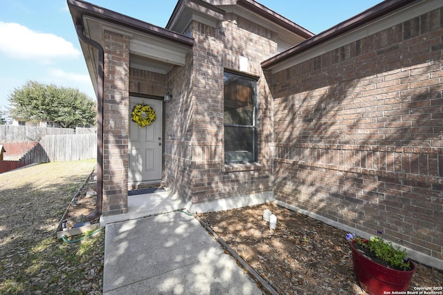 view of exterior entry with brick siding and fence