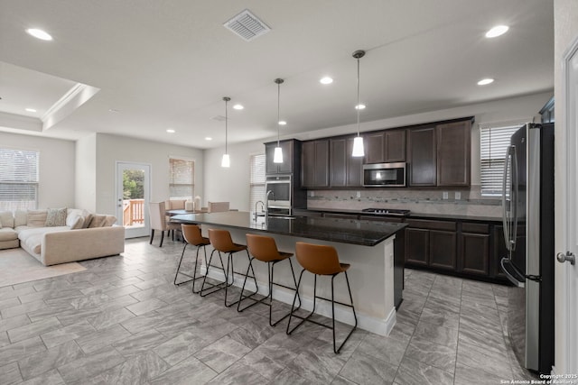 kitchen featuring pendant lighting, a breakfast bar, a kitchen island with sink, stainless steel appliances, and decorative backsplash