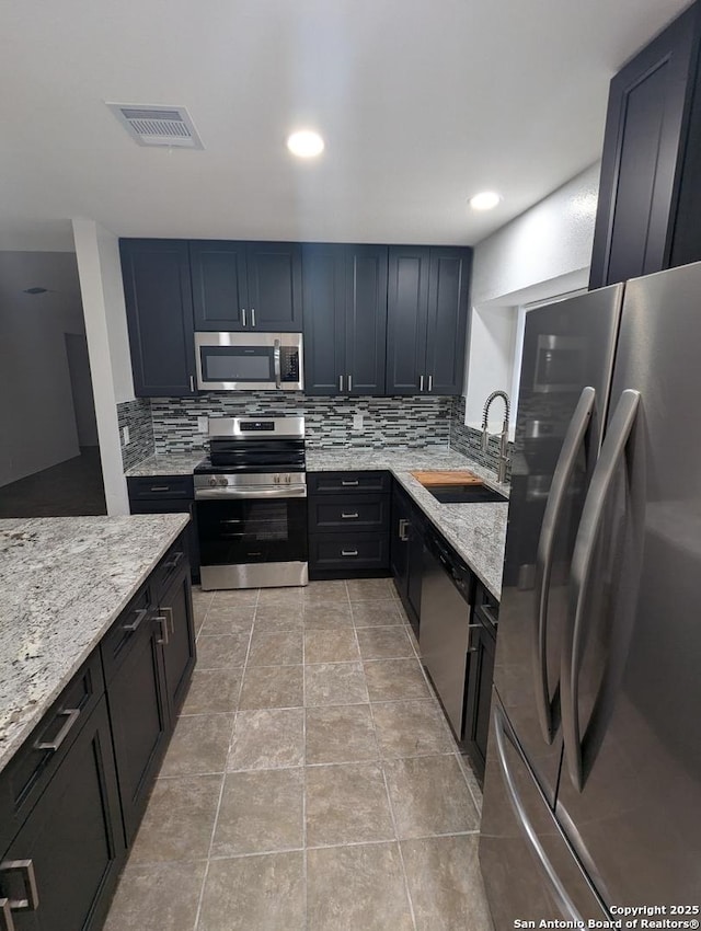 kitchen with sink, decorative backsplash, stainless steel appliances, and light stone countertops