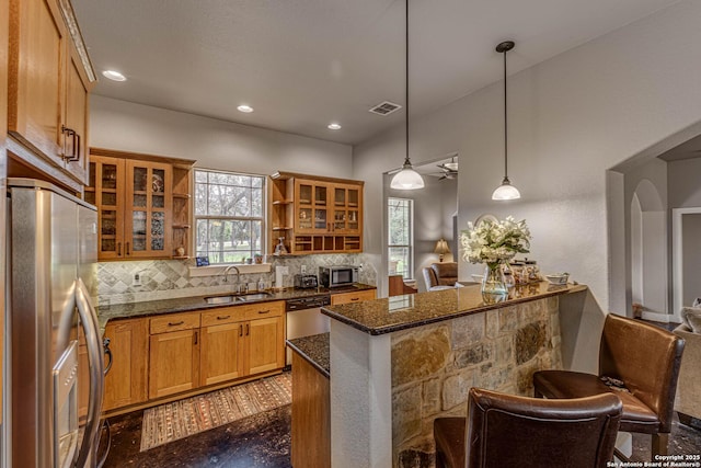 kitchen featuring sink, a breakfast bar area, dark stone counters, pendant lighting, and stainless steel appliances