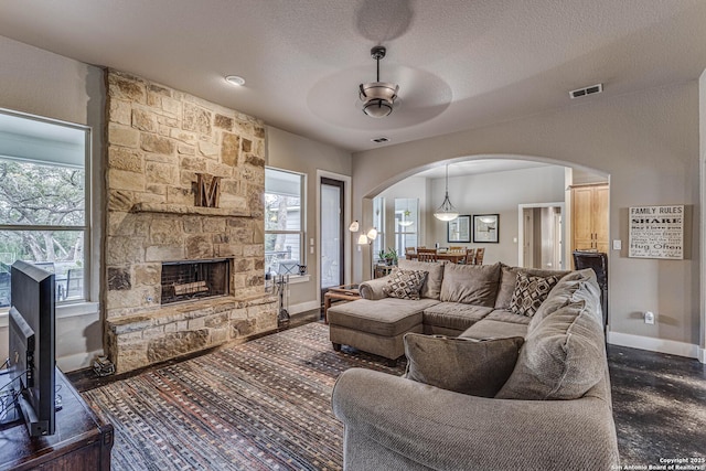 living room with ceiling fan, plenty of natural light, a textured ceiling, and a fireplace