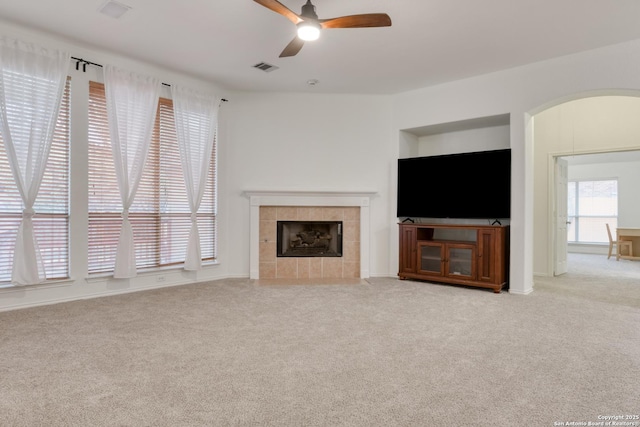 unfurnished living room featuring ceiling fan, a tile fireplace, and light carpet