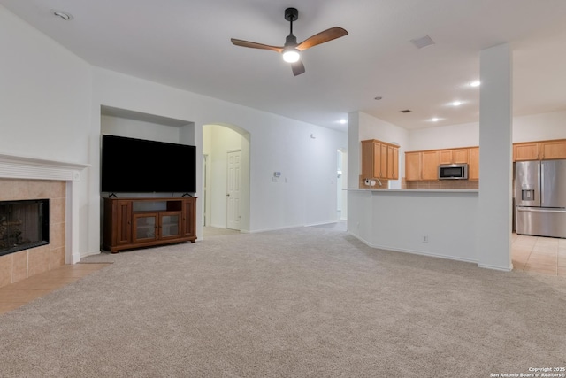 unfurnished living room featuring a tiled fireplace, light carpet, and ceiling fan