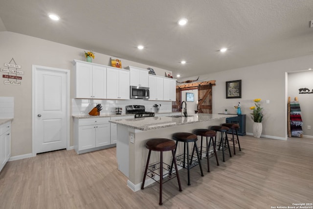 kitchen with appliances with stainless steel finishes, white cabinets, a kitchen breakfast bar, a kitchen island with sink, and a barn door