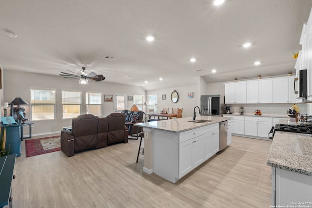 kitchen with light stone counters, appliances with stainless steel finishes, a center island with sink, and white cabinets