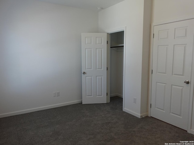 unfurnished bedroom with a walk in closet, a closet, and dark colored carpet