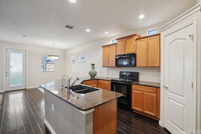 kitchen with sink, black appliances, an island with sink, dark hardwood / wood-style flooring, and dark stone counters