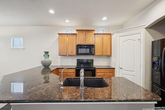 kitchen featuring sink, a kitchen island with sink, dark stone counters, and black appliances