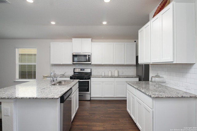 kitchen featuring sink, white cabinetry, stainless steel appliances, light stone countertops, and a kitchen island with sink