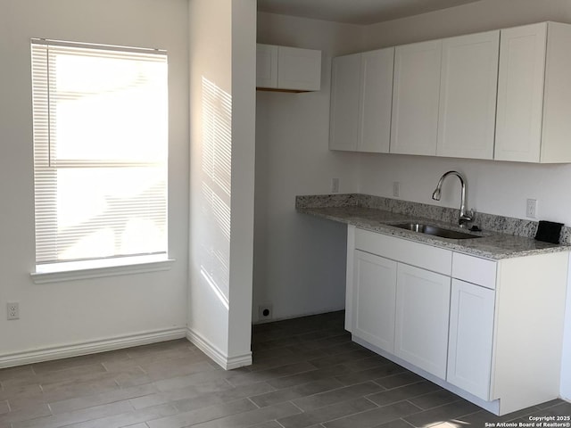 kitchen with white cabinetry, sink, and light stone counters