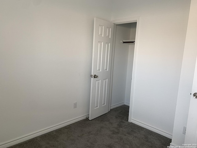 unfurnished bedroom with dark carpet and a closet