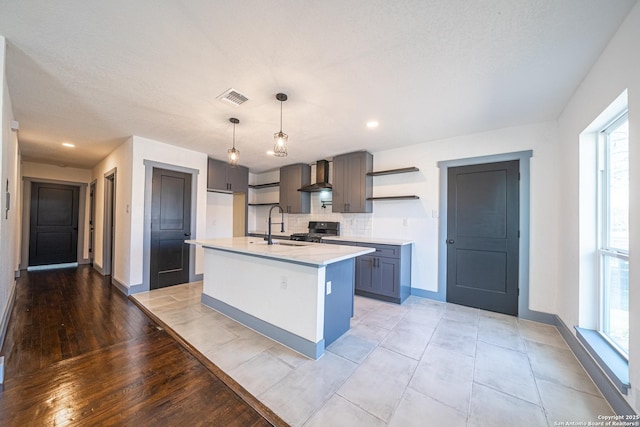 kitchen featuring pendant lighting, sink, stove, a center island with sink, and wall chimney exhaust hood