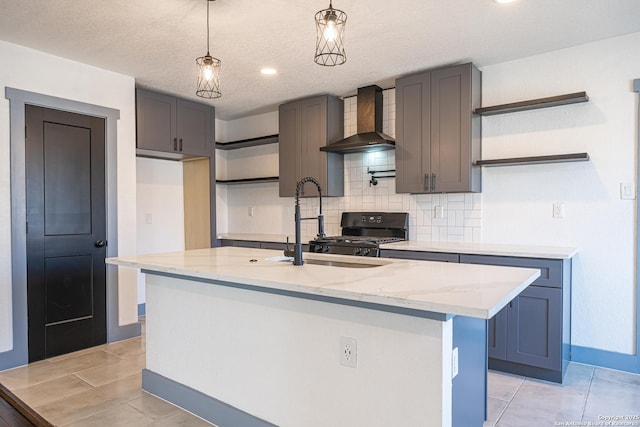 kitchen featuring wall chimney exhaust hood, decorative light fixtures, an island with sink, light stone countertops, and decorative backsplash