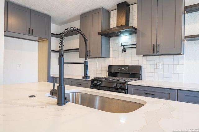 kitchen with black range with gas stovetop, wall chimney exhaust hood, light stone counters, and a textured ceiling