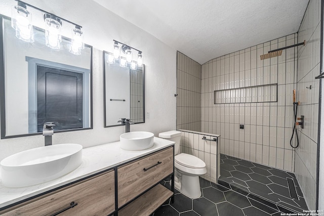 bathroom featuring toilet, a textured ceiling, a tile shower, vanity, and tile patterned flooring