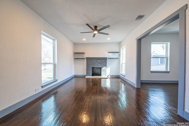 unfurnished living room with dark hardwood / wood-style flooring, ceiling fan, a stone fireplace, and a textured ceiling