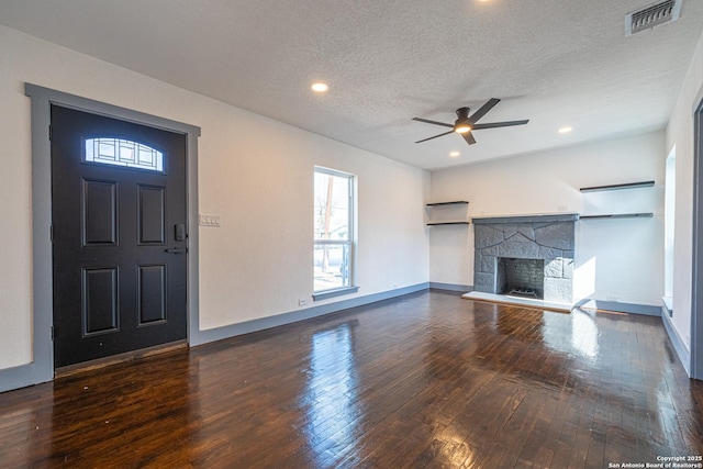 unfurnished living room with ceiling fan, a stone fireplace, dark wood-type flooring, and a textured ceiling