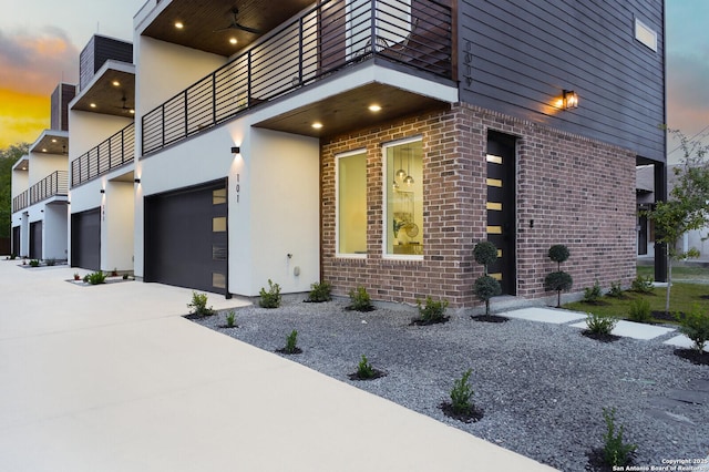 property exterior at dusk featuring a garage and a balcony