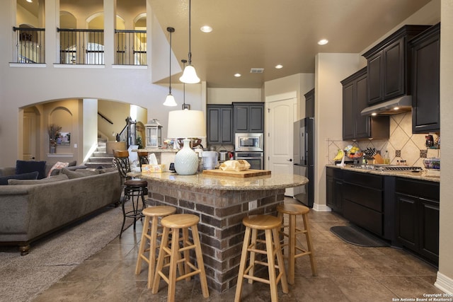 kitchen with appliances with stainless steel finishes, a kitchen breakfast bar, light stone counters, decorative backsplash, and decorative light fixtures