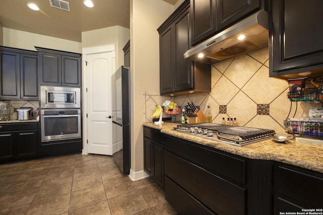 kitchen with tasteful backsplash, appliances with stainless steel finishes, light stone countertops, and dark tile patterned floors