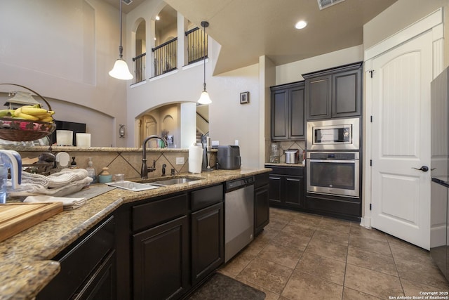 kitchen with sink, dark tile patterned floors, appliances with stainless steel finishes, backsplash, and decorative light fixtures