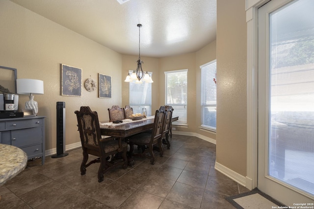 dining space with an inviting chandelier, dark tile patterned floors, and a textured ceiling