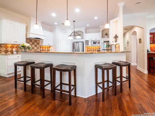 kitchen with white cabinetry, hanging light fixtures, stainless steel appliances, dark hardwood / wood-style floors, and light stone countertops