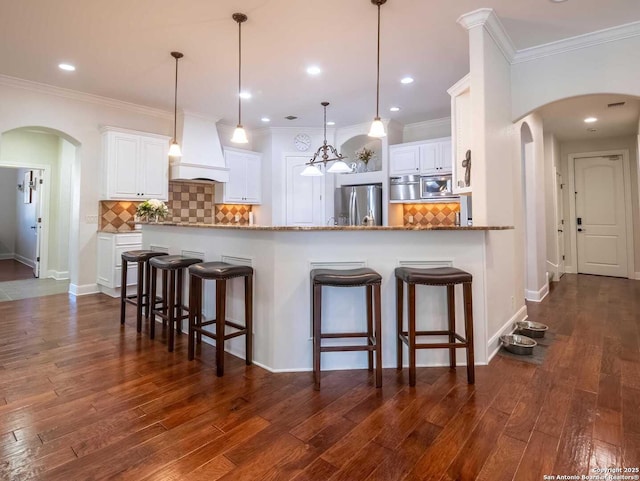 kitchen with light stone counters, appliances with stainless steel finishes, kitchen peninsula, custom range hood, and white cabinets