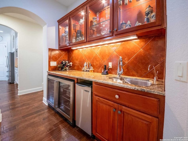 bar featuring stainless steel refrigerator, beverage cooler, light stone countertops, and sink