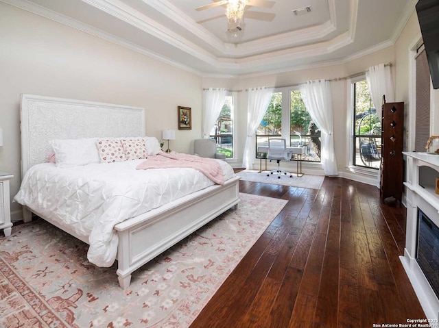 bedroom with multiple windows, a tray ceiling, ornamental molding, and dark hardwood / wood-style floors