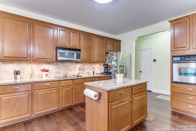 kitchen with tasteful backsplash, appliances with stainless steel finishes, dark hardwood / wood-style floors, a kitchen island, and light stone countertops