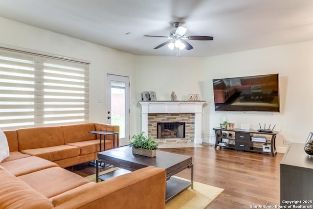 living room with hardwood / wood-style flooring, a stone fireplace, and ceiling fan