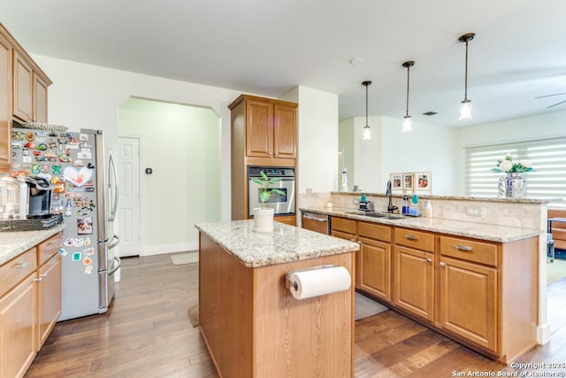 kitchen with sink, a kitchen island, pendant lighting, stainless steel appliances, and light stone countertops