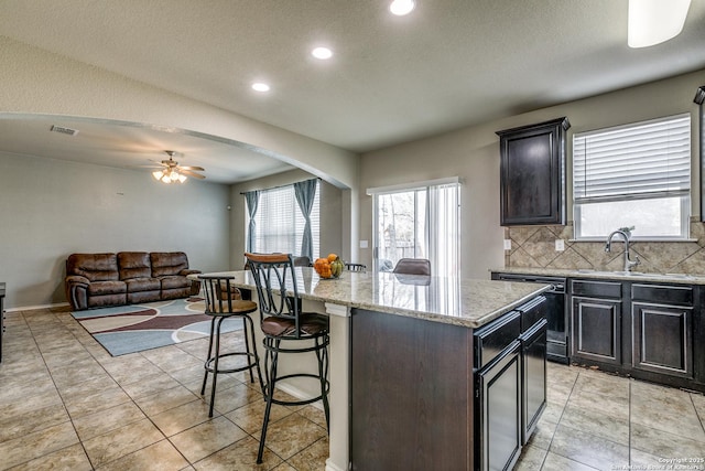 kitchen with a kitchen bar, sink, light stone counters, a center island, and backsplash